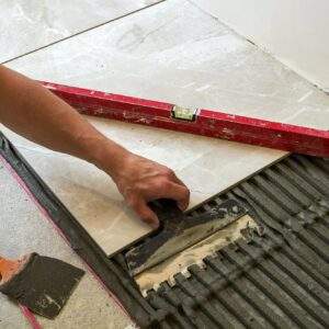 Ceramic tiles and tools for tiler. Worker hand installing floor tiles. Home improvement, renovation